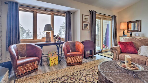 A cozy living room with a large window, a sofa, two leather armchairs, a coffee table with decorative items, and a patterned rug. - Cozy Mountain Getaway w/ Ski Shuttle Access! (Fraser)