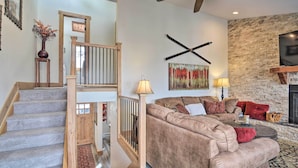 A staircase with wooden railings leading to a second floor, a living room with a beige sofa set, a fireplace, and a stone wall. - Cozy Mountain Getaway w/ Ski Shuttle Access! (Fraser)