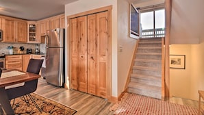 A kitchen with wooden cabinets, a stainless steel refrigerator, a dining table with chairs, and a staircase leading to a balcony. - Cozy Mountain Getaway w/ Ski Shuttle Access! (Fraser)