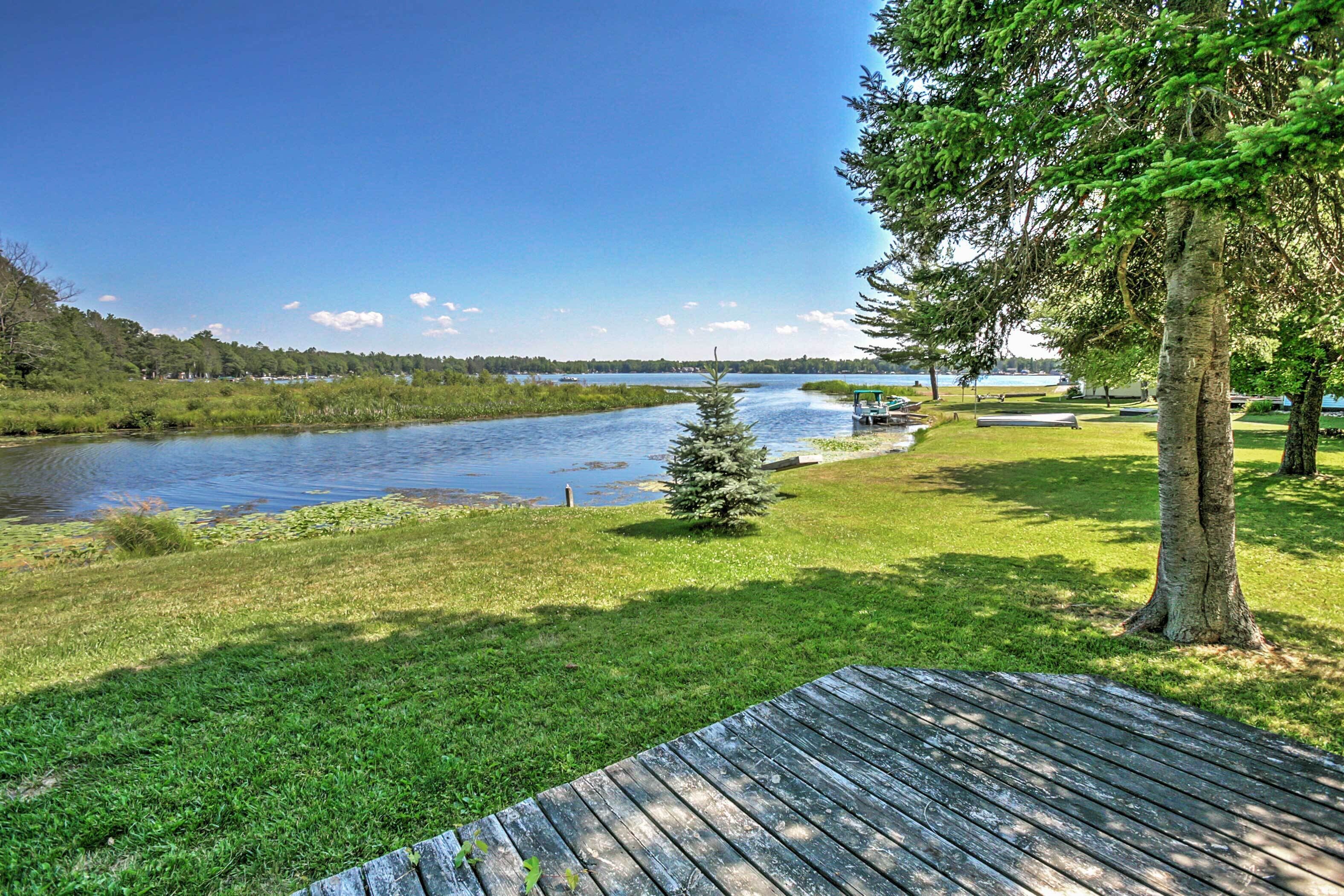 A riverside view with a wooden deck, grassy areas, and trees.