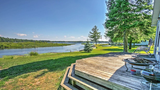 A wooden deck with a fire pit and grill, overlooking a river and a grassy area with trees. - 2 Mi to Boat Ramp! Family Cabin on Long Lake (Hale)