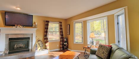 A living room with a fireplace, a sofa, a coffee table, and large windows.