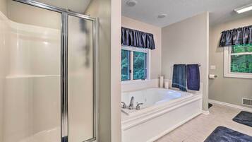 A bathroom with a walk-in shower, a freestanding bathtub, and two windows with dark curtains.