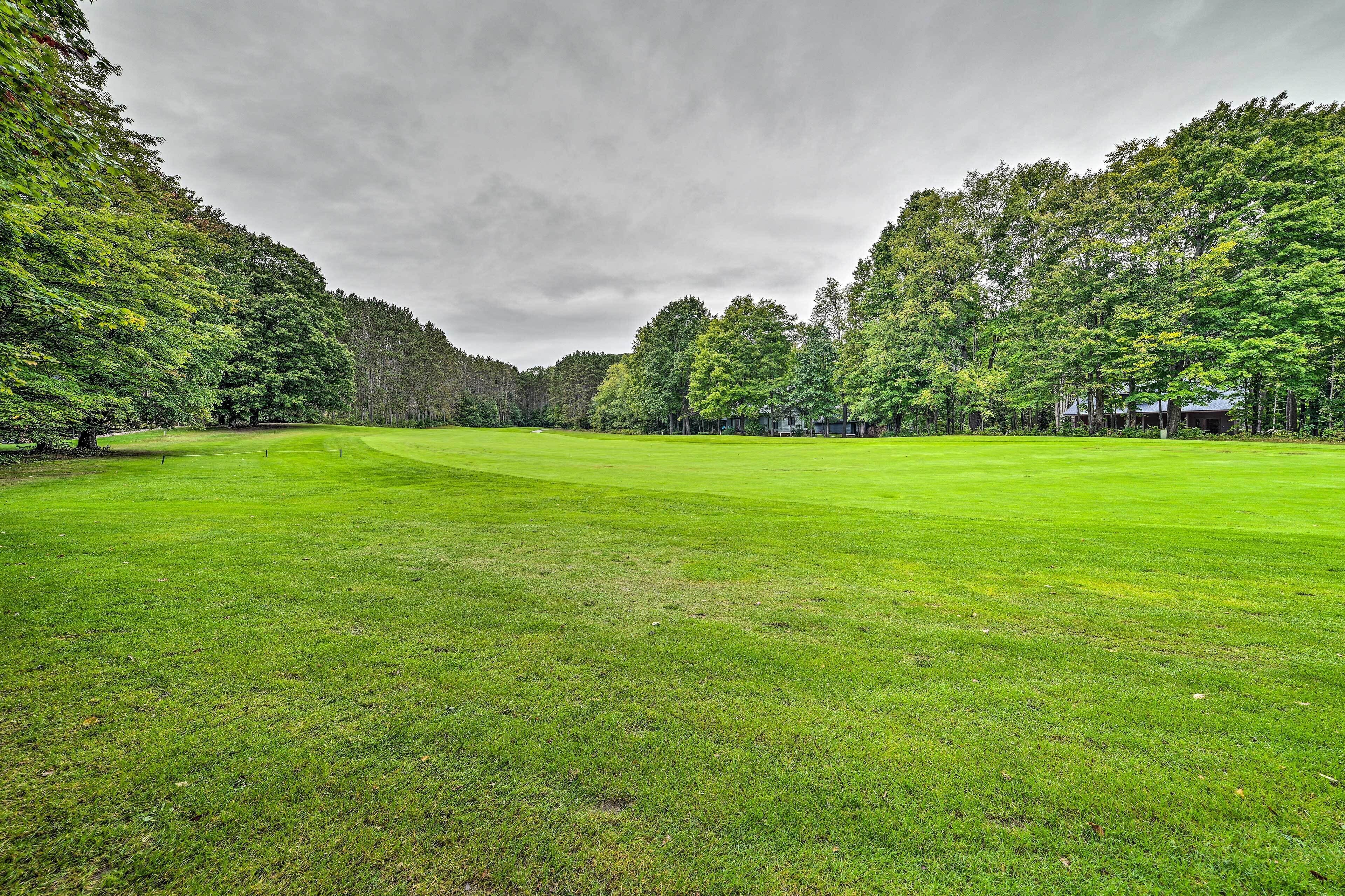 Un campo de golf con un césped bien cuidado, rodeado de árboles frondosos y un cielo nublado.