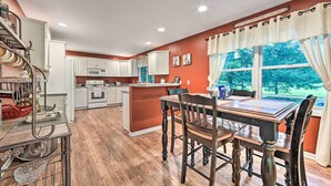 A kitchen with white cabinets, a wooden dining table, and a window with curtains. - Bellaire Ski Escape ~ 1 Mile to Schuss Mountain! (Bellaire)