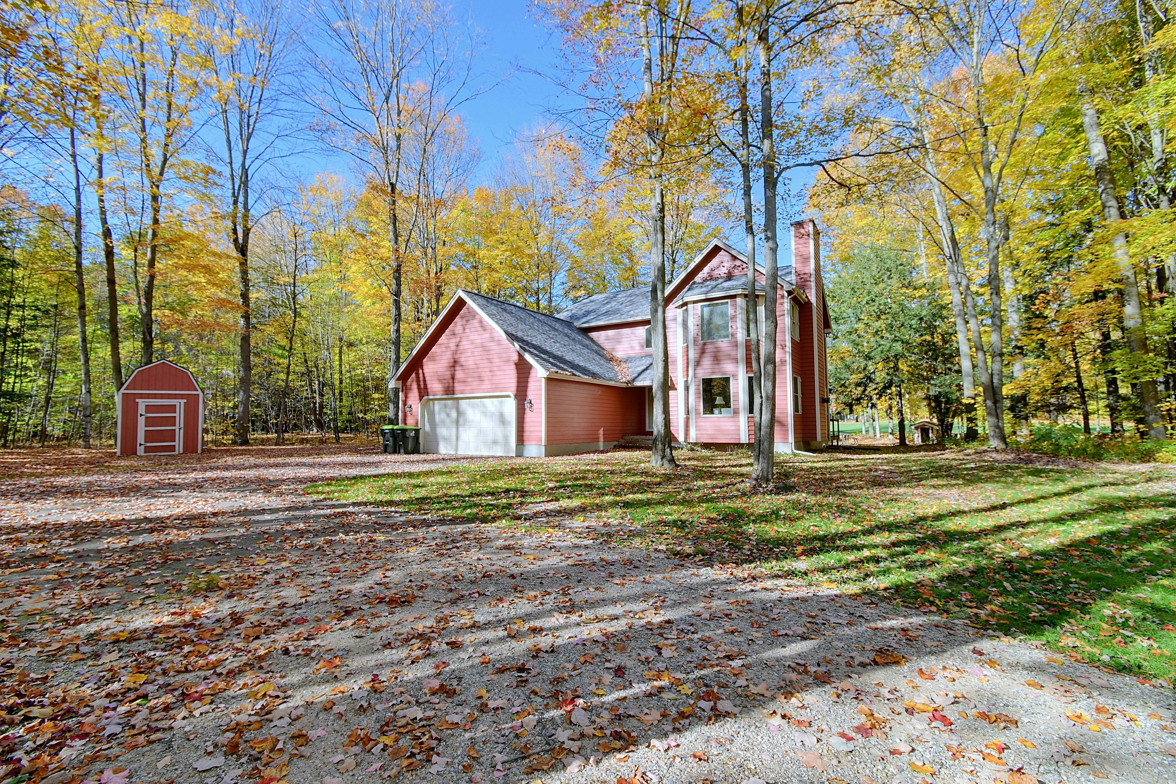 A red cabin with a garage, surrounded by a forest with autumn foliage.