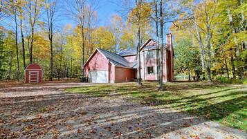 A red cabin with a garage, surrounded by a forest with autumn foliage.