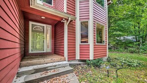 A red two-story house with a front porch, steps leading to the door, and a garden with a lawn and trees. - Bellaire Ski Escape ~ 1 Mile to Schuss Mountain! (Bellaire)