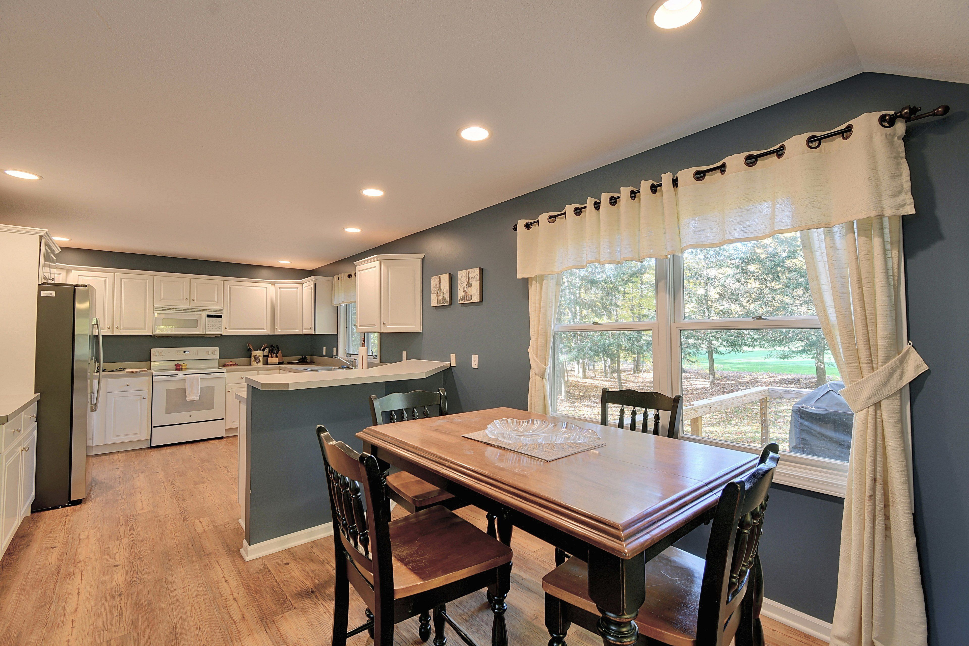A kitchen with white cabinets, a wooden dining table, and a window with curtains.
