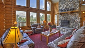 A log cabin interior with a stone fireplace, large windows, and a cozy seating area.