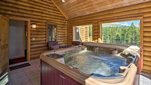 A log cabin interior with a hot tub, wooden walls, and a view of a forest.