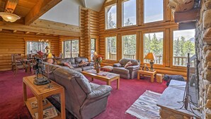 A log cabin interior with a large living area, multiple seating options, and a stone fireplace.