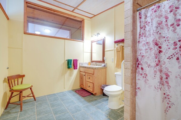 Un baño pequeño con una silla de madera, un lavamanos, un inodoro y una cortina de ducha.