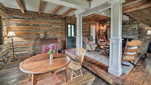 A rustic log cabin interior with a wooden dining table, chairs, and a stone fireplace. - Historic Virginia Wine Country Villa w/ Pool, Yard (Linden)