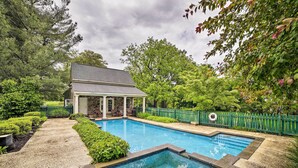 A rectangular swimming pool with a stone border, surrounded by a stone pathway and lush greenery. - Historic Virginia Wine Country Villa w/ Pool, Yard (Linden)