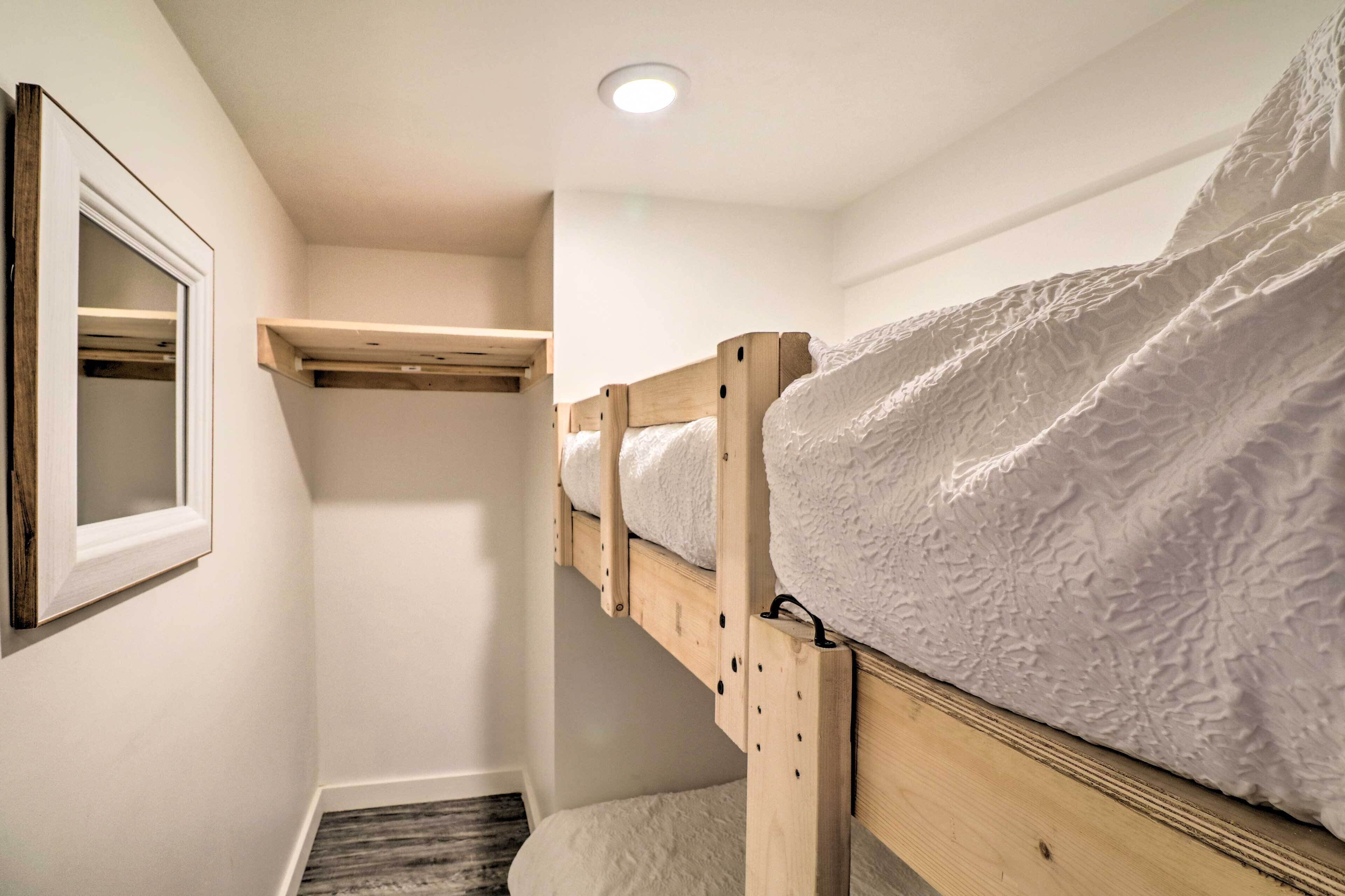 Een stapelbed met houten frame en witte beddengoed, een klein plankje erboven en een lijst met spiegel aan de muur.