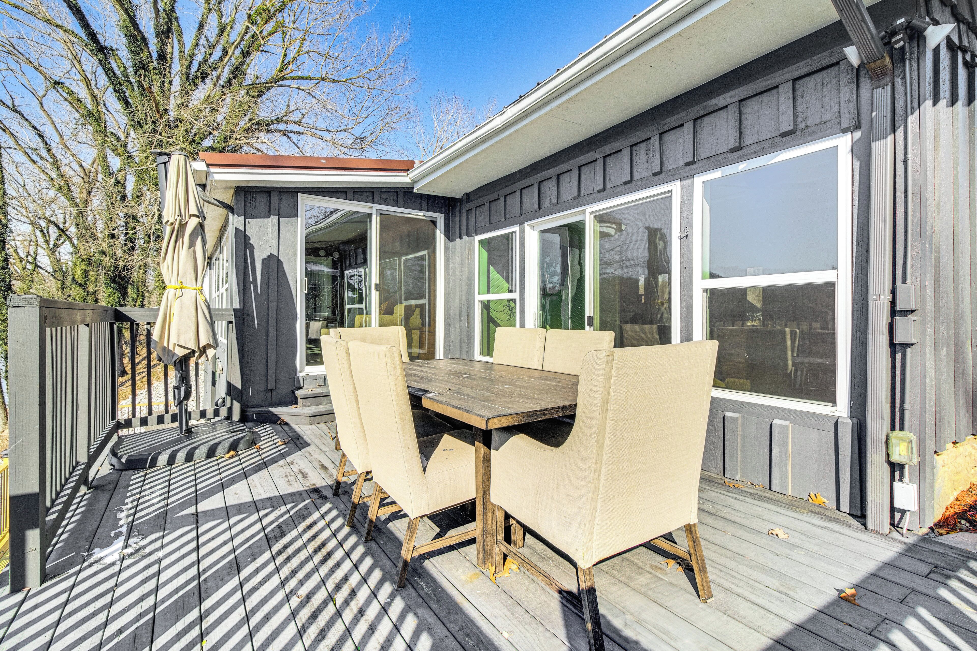 A deck with a wooden table and chairs, a covered patio area, and large windows.