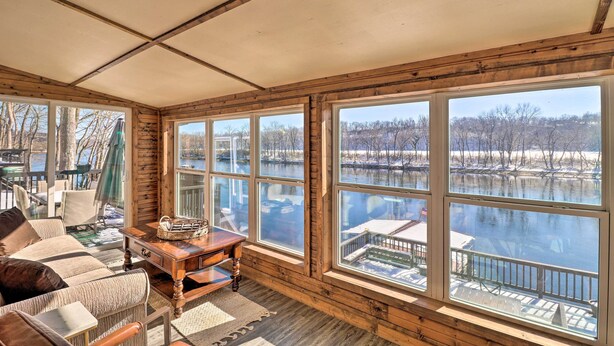 A cozy room with large windows overlooking a lake, wooden walls, and a comfortable seating area. - 'fish House' w/ Deck, Fire Pit & River Views (Cotter)