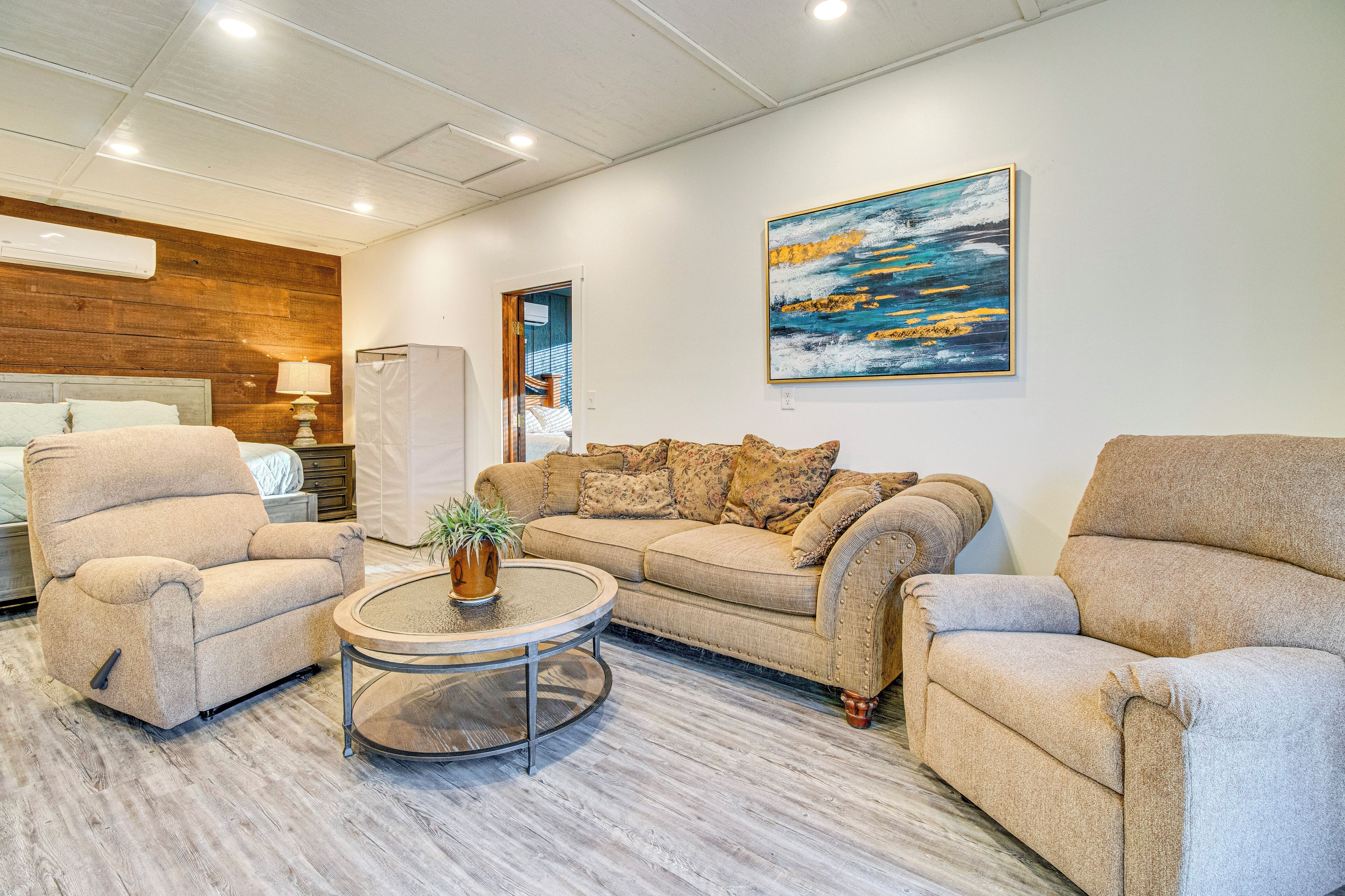 A modern living room with a beige sofa, two armchairs, a round coffee table, and a painting on the wall.