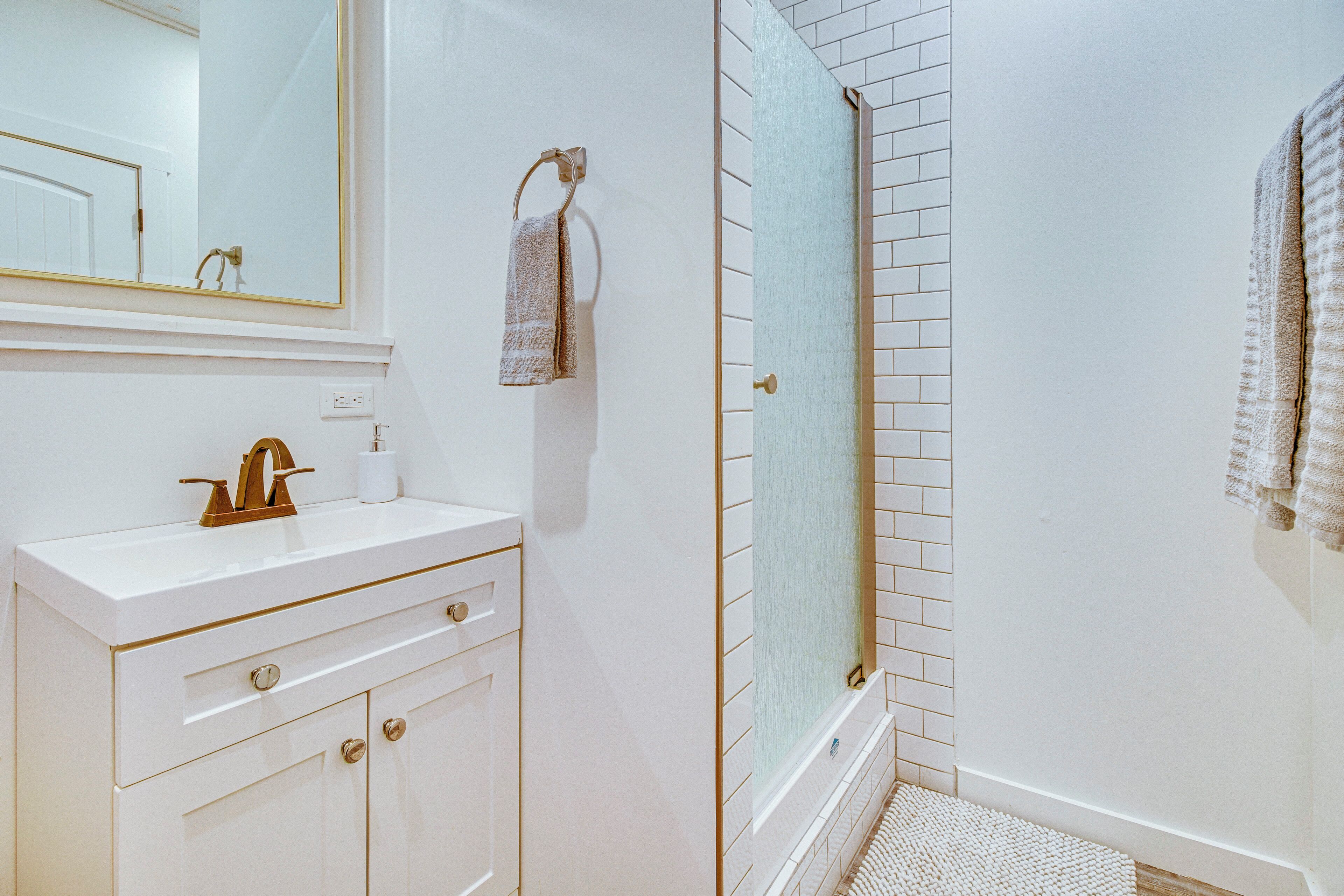 Un bagno con un mobile lavabo bianco, un portascopino, una doccia con porta in vetro e zona doccia rivestita in piastrelle.