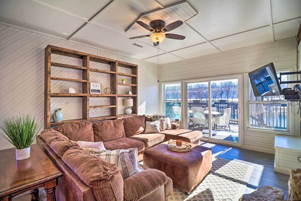 A cozy living room with a large wooden bookshelf, a brown leather sofa, and a ceiling fan. - 'fish House' w/ Deck, Fire Pit & River Views (Cotter)