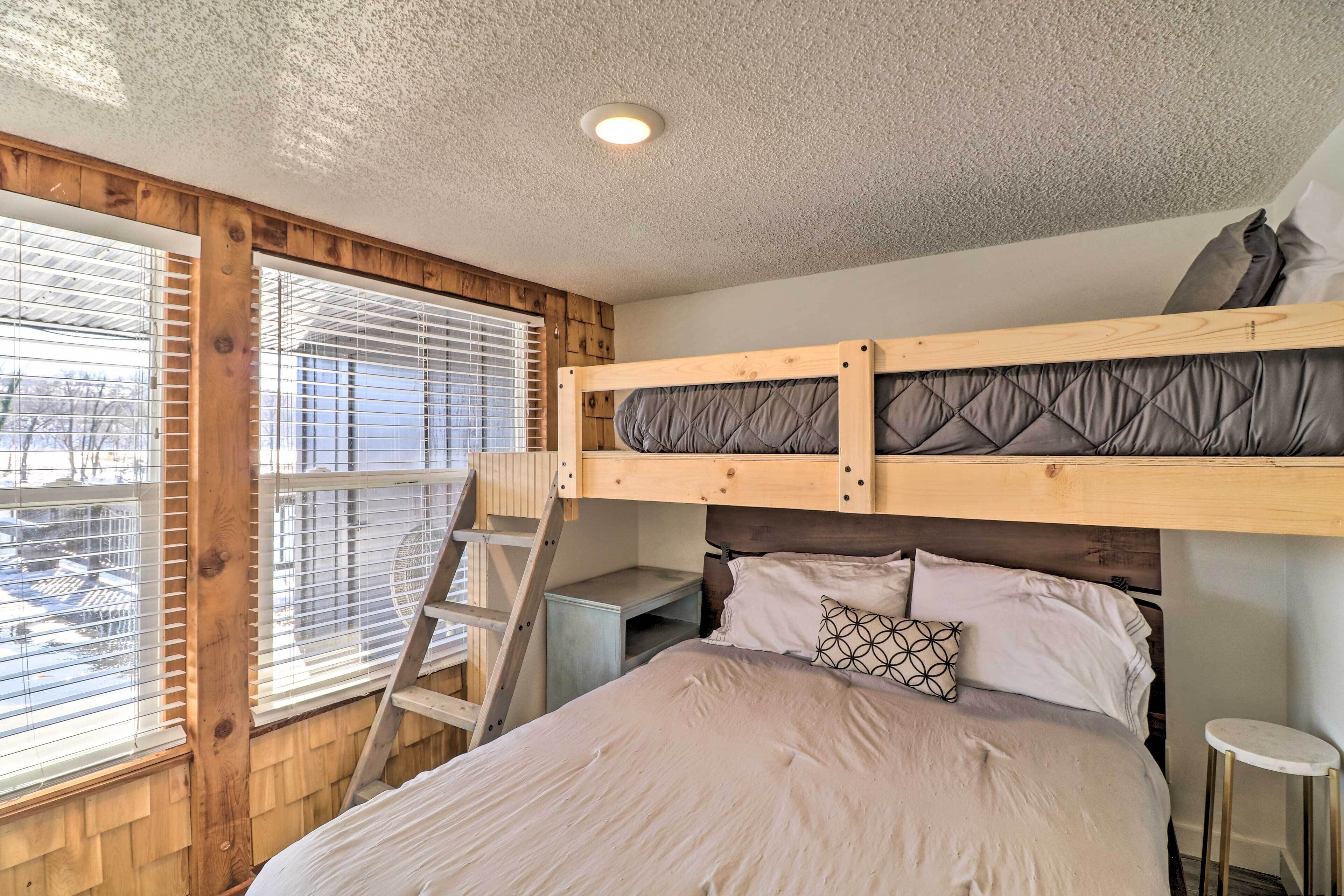 A bunk bed with a ladder, a desk, and a window with blinds.