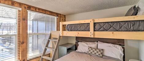 A bunk bed with a ladder, a desk, and a window with blinds.