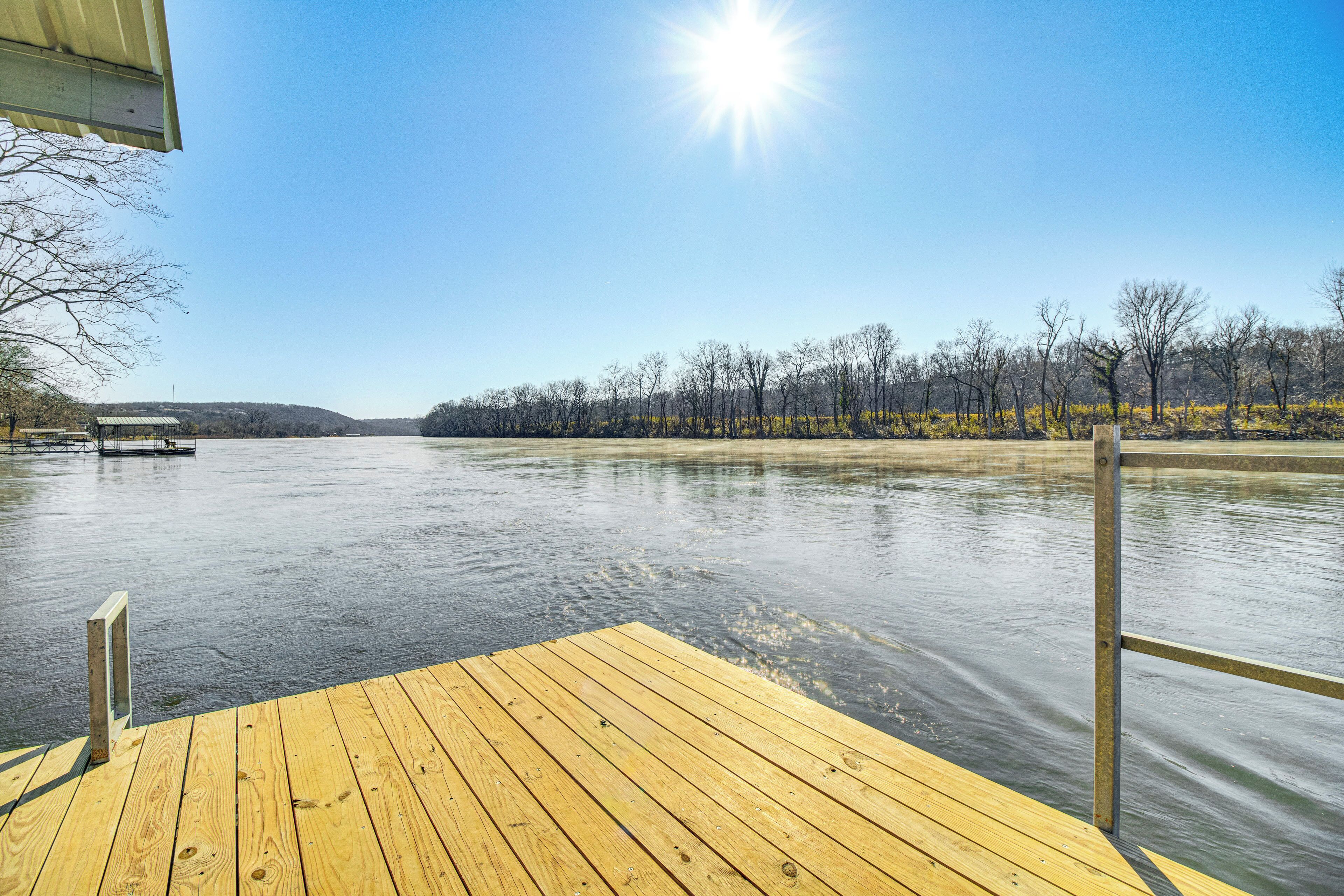 A wooden dock extending into a calm river with a clear sky above.