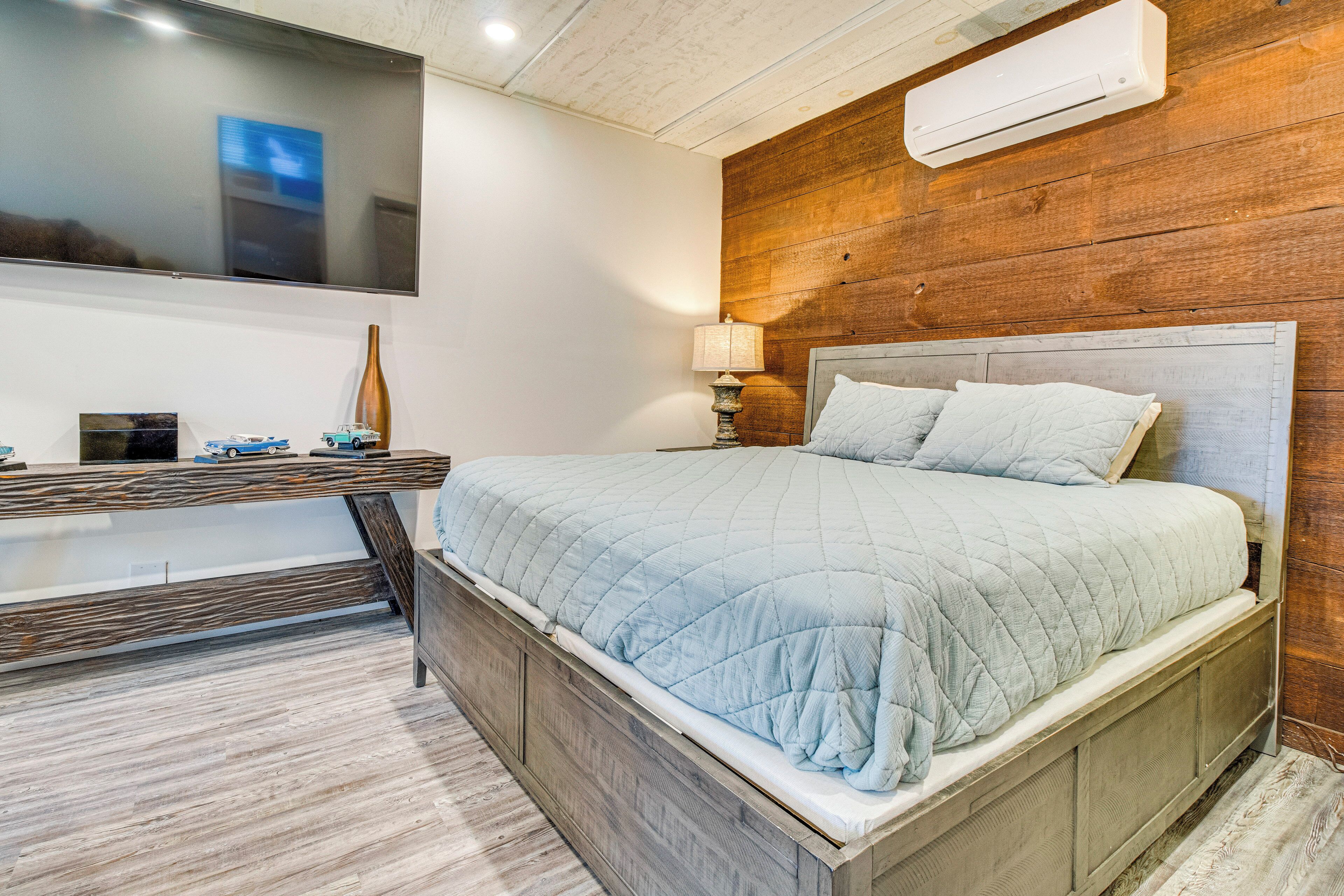 A bedroom with a wooden headboard, a bed with a quilted blanket, a bedside table with a lamp, and a TV mounted on the wall.