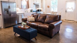 A modern kitchen with white cabinets, stainless steel appliances, and a brown leather sofa with a blue ottoman. - Dog-friendly Texas Ranch w/ Patio, Horses On-site (Aubrey)