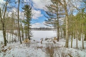 A snow-covered landscape with a cabin and outdoor seating area surrounded by trees. - Fish, Hike & Hunt: Lakeside Newaygo Cottage (Newaygo)