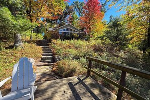 Eine Holzterrasse führt zu einem Haus, das von Herbstlaub umgeben ist.