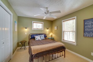 A bedroom with a bed, a ceiling fan, two windows with blinds, a bedside table with a lamp, and a wall with a framed inspirational quote. - Fish, Hike & Hunt: Lakeside Newaygo Cottage (Newaygo)