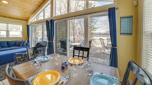 A dining area with a wooden table set for four, a blue and yellow tablecloth, and a view of a deck and trees outside. - Fish, Hike & Hunt: Lakeside Newaygo Cottage (Newaygo)