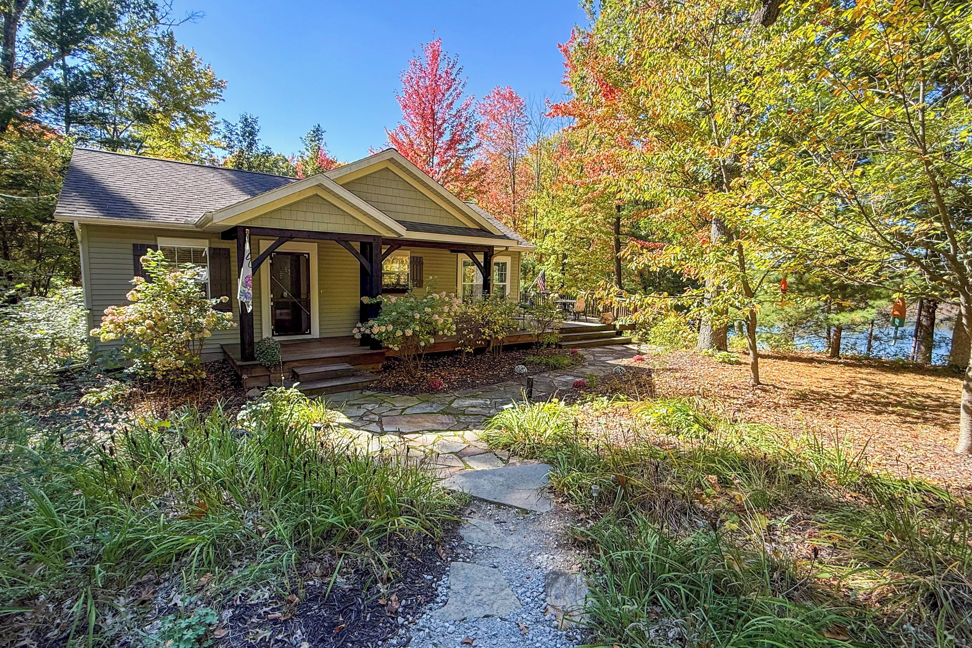 A two-story house with a porch, a stone pathway leading to the entrance, and a garden with various plants and shrubs.