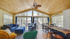 A spacious living room with a high ceiling, large windows, a wooden ceiling fan, and a bar area with stools. - Fish, Hike & Hunt: Lakeside Newaygo Cottage (Newaygo)
