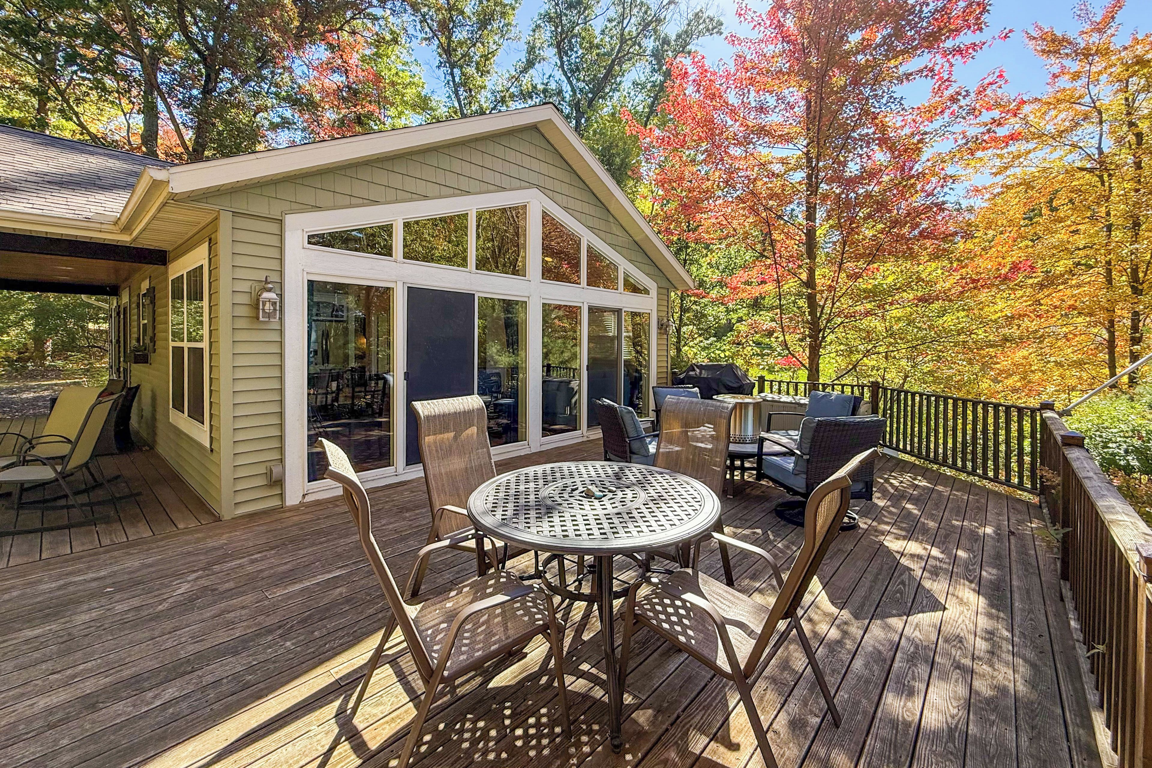 A covered outdoor patio with a table and chairs, a small building with large windows, and a wooden deck.
