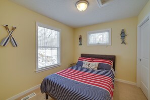 A bedroom with a bed, two windows, and wall decorations. - Fish, Hike & Hunt: Lakeside Newaygo Cottage (Newaygo)