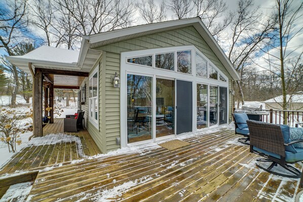 A covered deck with a wooden floor and a glass door leading to a patio area. - Fish, Hike & Hunt: Lakeside Newaygo Cottage (Newaygo)