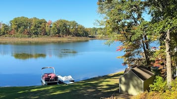 A calm lake with a boat docked on the shore, a shed, and trees in the background.