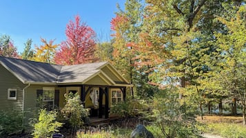 A single-story house with a porch, surrounded by a garden with various plants and trees displaying autumn colors.