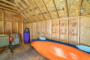 A room with wooden walls and a sloped ceiling, containing a kayak and a paddleboard. - Fish, Hike & Hunt: Lakeside Newaygo Cottage (Newaygo)
