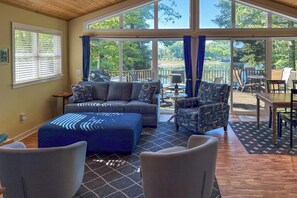 A spacious living area with a large window, a sofa, a coffee table, and a patterned rug. - Fish, Hike & Hunt: Lakeside Newaygo Cottage (Newaygo)