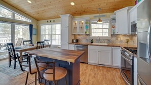 A spacious kitchen with wooden ceiling, white cabinets, a central island, and a dining area with chairs. - Fish, Hike & Hunt: Lakeside Newaygo Cottage (Newaygo)