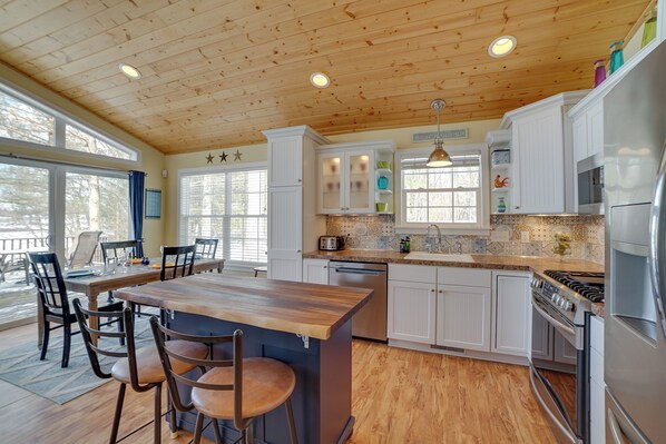 A spacious kitchen with wooden ceiling, white cabinets, a central island, and a dining area with chairs. - Fish, Hike & Hunt: Lakeside Newaygo Cottage (Newaygo)