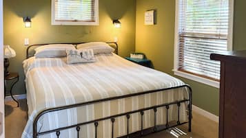 Un dormitorio con una cama, dos lámparas de pared, un ventanal con persianas y una mesita de noche con lámpara.