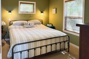 Un dormitorio con una cama, dos lámparas de pared, un ventanal con persianas y una mesita de noche con lámpara.