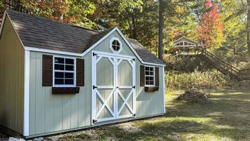 A small, single-story shed with a gabled roof, a central door, and two windows on each side.