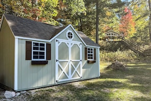 A small, single-story shed with a gabled roof, a central door, and two windows on each side. - Fish, Hike & Hunt: Lakeside Newaygo Cottage (Newaygo)