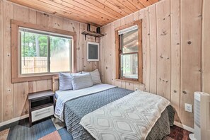 Quarto com painéis de madeira, uma cama, mesa de cabeceira e uma janela.